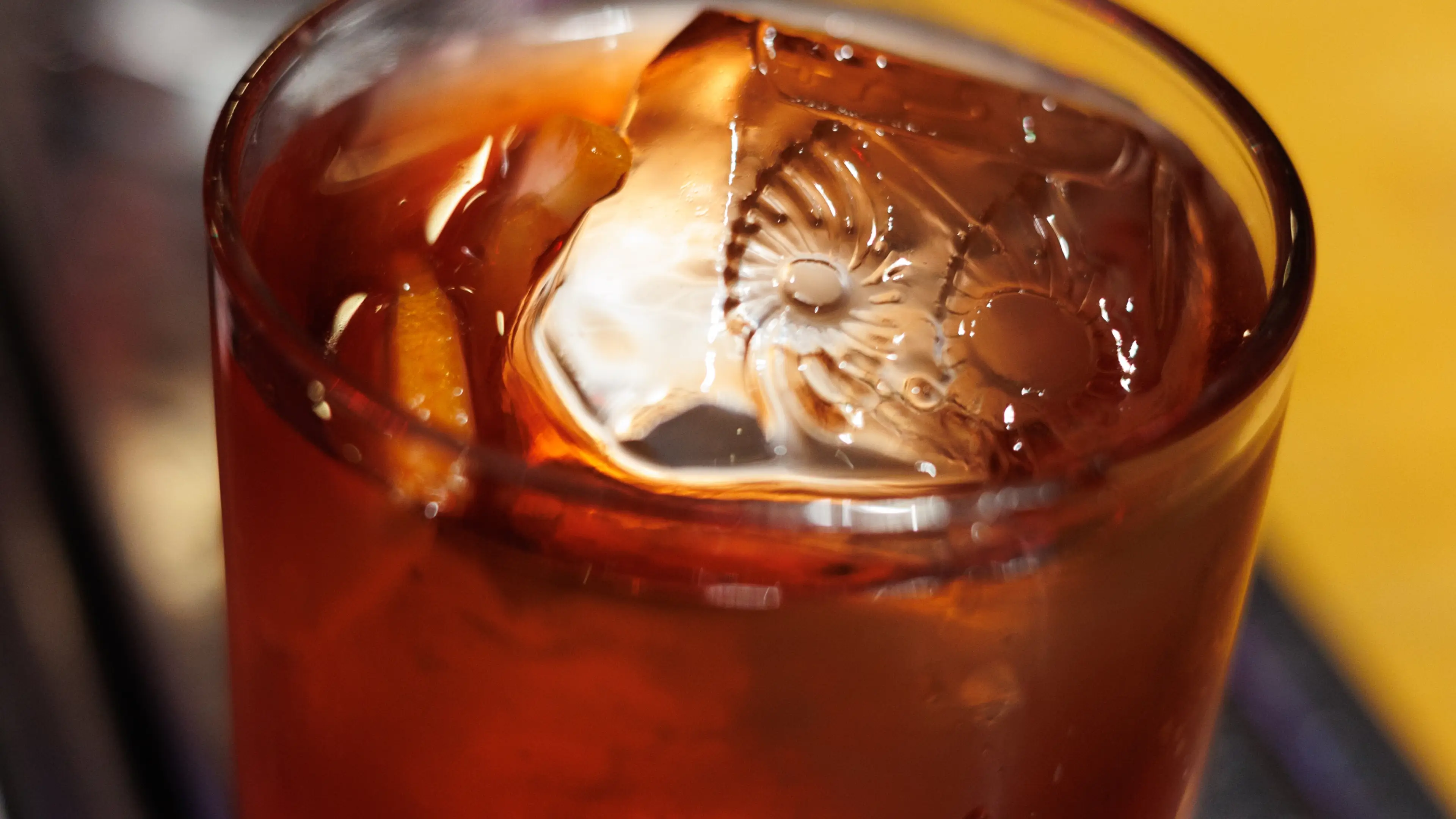 Foto bem próxima e detalhada de um drink do OIDĒ em copo de vidro. Na superfície um cubo de gelo com a gravação do símbolo do OIDĒ.